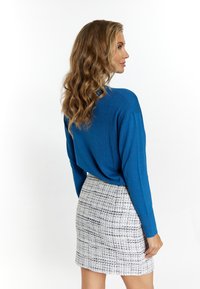 Maglione blu a maglia con maniche lunghe abbinato a una gonna a quadretti bianca e blu testurizzata. Sfondo bianco semplice.
