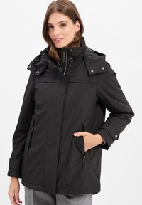 Schwarze wasserdichte Jacke mit hohem Kragen, Druckknöpfen und Reißverschluss-Taschen. Verfügt über ein gesteppte Design und eine abnehmbare Kapuze.