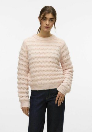 Helles rosa Sweatshirt mit einer wellenförmigen Textur, Rundhalsausschnitt und gerippten Bündchen. Kombiniert mit dunkelblauen Jeans. Weicher, gestrickter Stoff.