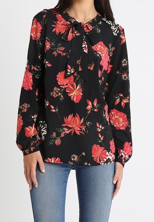 Czarna bluzka z długim rękawem z czerwonym i różowym kwiatowym wzorem, z detalem wiązania przy szyi, noszona z niebieskimi dżinsami.