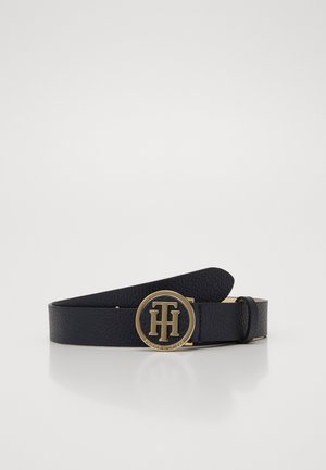Ceinture en cuir noir texturé avec boucle ronde dorée présentant le logo TH entrelacé et le nom de la marque gravé sur fond blanc.
