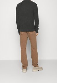 Mörk texturerad tröja med ribbad detaljer, matchad med ljusbruna byxor och beige skor. Outfiten har en avslappnad design.