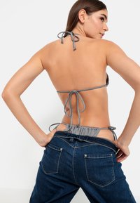 Γκρίζο μπικίνι με κορδόνια πίσω, συνδυασμένο με ξεφτισμένο σκούρο μπλε τζιν με ελαστική μέση και τσέπες.