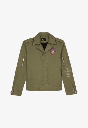 Veste militaire de couleur vert olive, en tissu coton, poches avant, poches latérales à fermeture éclair, détail de badge sur la poitrine gauche, texte sur la manche droite.