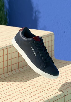 Navy blue leather sneaker with white rubber sole, featuring dark laces, red accents at the heel, and a logo on the side.