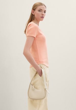 Top rosa a righe con maniche corte abbinato a pantaloni beige a vita alta; una piccola borsa a tracolla color crema con dettagli in zip poggia sul lato.