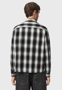 Czarna i biała koszula flanelowa w kratę z zapięciem na guziki, o prostym kroju i długich rękawach, prezentowana z tyłu.
