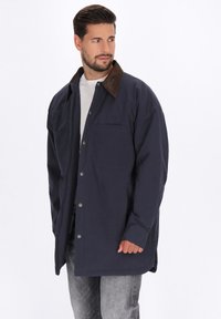 Marinejacke mit braunem Cordkragen, mit Knopfleiste, einer Brusttasche und lockerem Schnitt. Weicher Stoff und strukturierte Details.