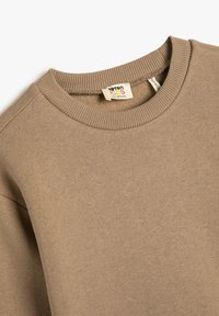 Sudadera de algodón beige para niños con cuello redondo, cuello de canalé y textura sutil, que incluye una etiqueta en el interior del cuello.