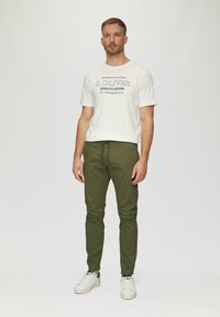 Witte katoenen T-shirt met "S. Oliver Quality Goods" in donkergrijs gedrukt, gecombineerd met olijfgroene, taperende enkelbroeken en witte sneakers.