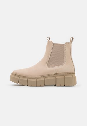 Botte Chelsea beige avec semelle en caoutchouc épaisse, panneaux latéraux élastiques, languettes à la cheville et finition mate lisse.