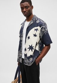 Μπλούζα κοντό μανίκι σε ναυτικό μπλε και εκρού, με σχέδια αστεριών και λουλουδιών, κατασκευασμένη από απαλή ύφανση, με χαλαρή εφαρμογή και ανοιχτό γιακά.