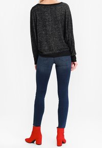 Czarny sweter o teksturowanej powierzchni w luźnym kroju, połączony z niebieskimi skinny jeansami i czerwonymi botkami z blokowym obcasem.