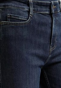 Granatowe dżinsy o gładkiej fakturze, z przednią kieszenią i żółtymi przeszyciami. Klasyczny krój i prosty fason.