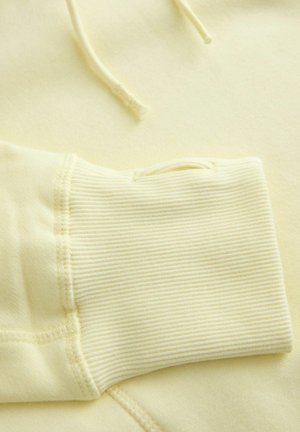 Žlutá mikina z tkaniny s žebrovanými manžetami, ukazující hladkou strukturu a šňůrky. Vyznačuje se měkkým, lehkým materiálem pro pohodlí.