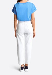 Blå bomullströja med uppvikta ärmar, kombinerad med högmidjade vita jeans och vita sneakers med marinblå detaljer.