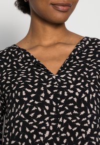 Vestido preto com padrão, featuring decote em V e pequenas formas brancas semelhantes a folhas. Feito de um tecido suave com uma aparência texturizada.