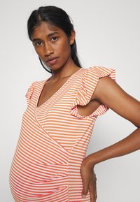 Blusa de maternidade em laranja e branco com riscas horizontais, apresentando mangas em babados e um decote em V com uma silhueta ajustada.