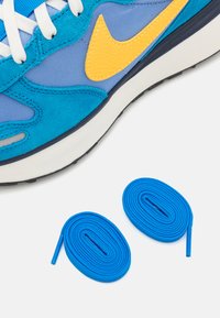 Sapatilhas azuis e verde-água com um swoosh amarelo da Nike, apresentando texturas de camurça e malha. Dois atacadores azuis estão debaixo.