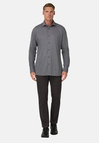 Szary, zapinany na guziki koszula z kołnierzykiem, długimi rękawami i prostym krojem. Połączona z ciemnymi spodniami i czarnymi sneakersami.