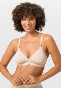 Beige kabelloser BH mit dreieckigem Design, weichem Stoff, verstellbaren Trägern und breitem Unterband für Unterstützung. Glatte Textur, minimale Details.