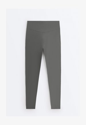 Grijze, hoogtailige legging met een naadloos ontwerp en taps toelopende pijpen, weergegeven op een effen witte achtergrond.