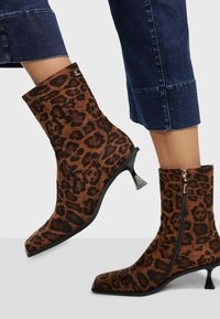 Botas de tobillo de estampado de leopardo hechas de tela suave, con punta afilada y un tacón corto y curvado, con un cierre de cremallera lateral.