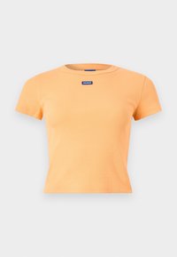 Crop top orange à manches courtes en maille côtelée avec encolure ronde et petite écusson rectangulaire bleu situé sous le col au centre.