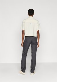 Kort ljusbeige skjorta med korta ärmar, med en logotyp på baksidan, kombinerad med mörkgrå cargobyxor med fickor.