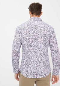 Langärmeliges Hemd mit weißem Hintergrund, versehen mit einem kleinen Blumenmuster in Blau und Braun, Knopfleiste mit Kragen und abgerundetem Saum.