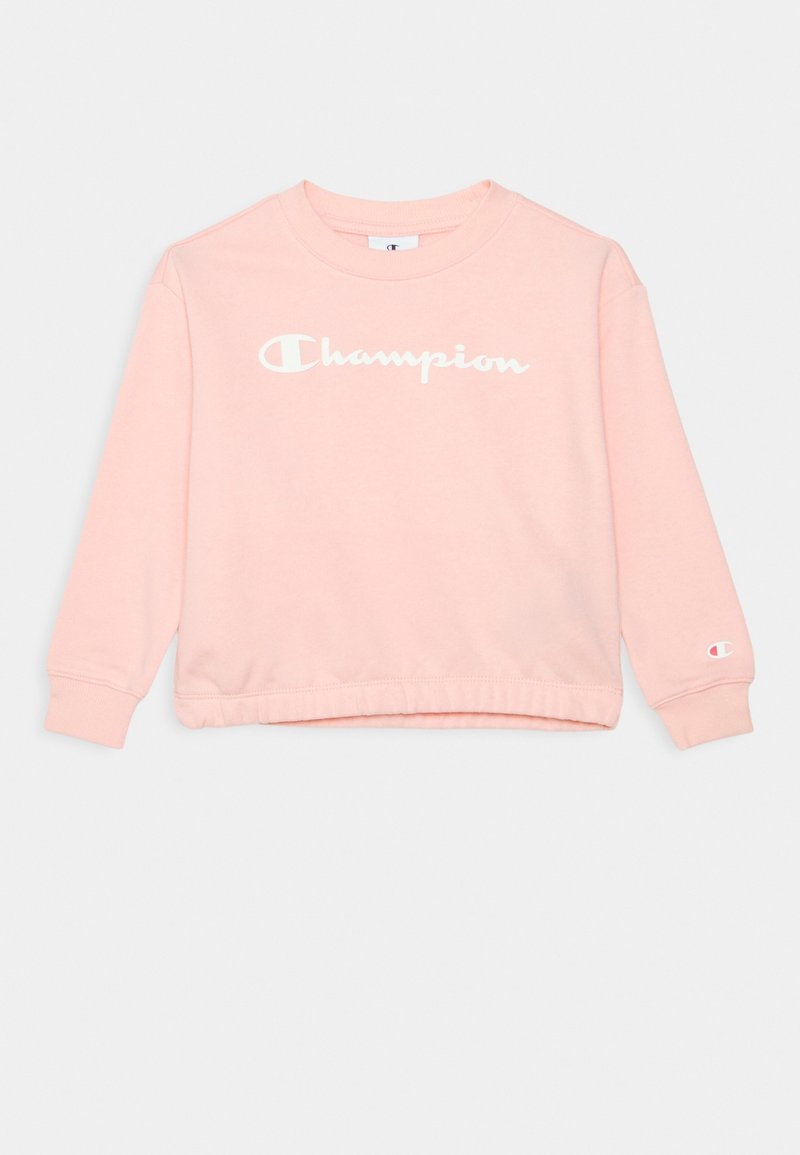 Sweat-shirt à manches longues rose clair avec le logo blanc "Champion" sur la poitrine et un petit logo "C" sur le poignet de la manche gauche.