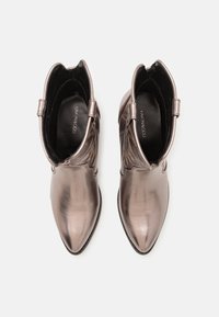 Par de botas metálicas de tacón con punta afilada y bordes en forma de ondas, con plantillas negras visibles de la marca Even&Odd, mostradas desde arriba sobre un fondo blanco.