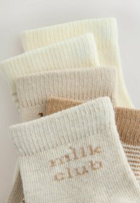 Cuatro pares de calcetines de punto acanalado doblados en tonos crema, beige y marrón, con un par que muestra el texto "wnlne club" en hilo beige.