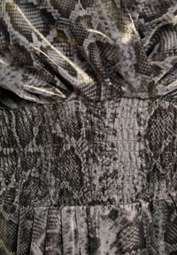 Tissu en motif de peau de serpent gris et noir avec une finition brillante, présentant une texture froncée et des détails plissés au niveau de l'ourlet.