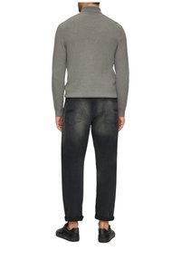 Grijze gebreide trui met een hoge kraag, gecombineerd met donkerdenim jeans met een lichte vervaging en opgerolde mouwen, gedragen met zwarte schoenen.