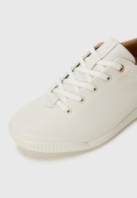 Sneaker en cuir blanc texturé avec des lacets blancs, bout rond et doublure intérieure beige clair sur un fond blanc.