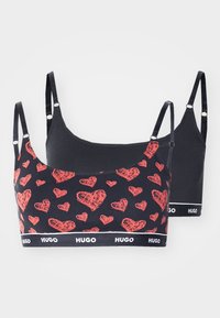 To crop tops i svart stoff. Den ene har et rødt hjerte-mønster, mens den andre er ensfarget svart. Begge har justerbare stropper og belter med logo.