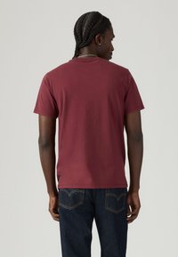 Bordeaux-rotes T-Shirt mit kurzen Ärmeln in lockerer Passform, mit Rundhalsausschnitt und weichem Baumwollstoff. Glatte Textur und keine sichtbaren Muster oder Beschläge.