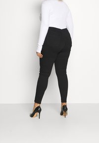 Svarta smala jeans med hög midja, bakfickor och en slät textur. Tillsammans med svarta högklackade skor och en vit långärmad topp.