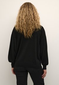 Sort oversized sweater med lange, puffede ærmer og ribbede manchetter. Blød tekstur, rund kant og minimal detaljering på bagsiden.