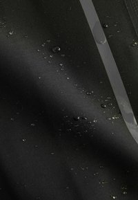 Tissu noir résistant à l'eau avec des gouttelettes d'eau dispersées et une bande réfléchissante verticale traversant le côté droit du tissu.