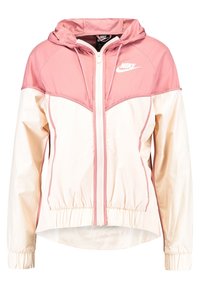 Rosa och krämfärgad Nike vindjacka med huva, vit dragkedja fram, elastiska ärmslut och Nike-logotyp på vänster bröst.