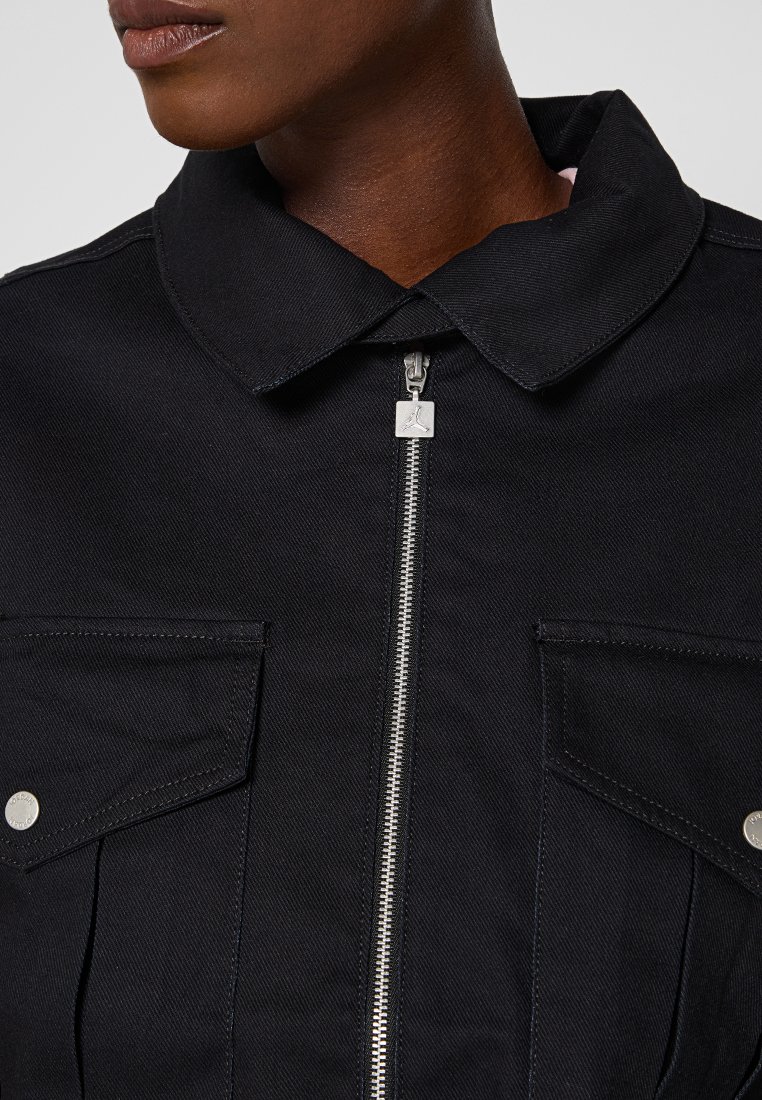 Giacca in denim nero con colletto a punta, zip argentata e due tasche sul petto con bottoni metallici. Materiale testurizzato con design su misura.