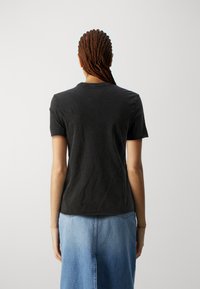 T-shirt nera a maniche corte realizzata in materiale morbido, con collo a giro, taglio dritto e cuciture minimal, abbinata a una gonna in denim blu.