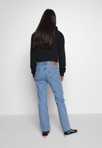 Jeans in denim blu con taglio a gamba dritta e toppa posteriore; abbinati a una felpa nera con cappuccio e sneaker nere. Tessuto liscio e design classico.