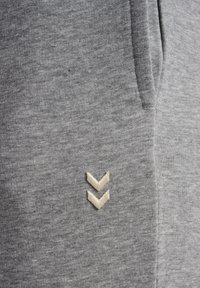 Graue Strick-Jogginghosen aus strukturiertem Material mit Seitentaschen und einem beige gestickten Chevron-Logo auf der linken Vorderseite.