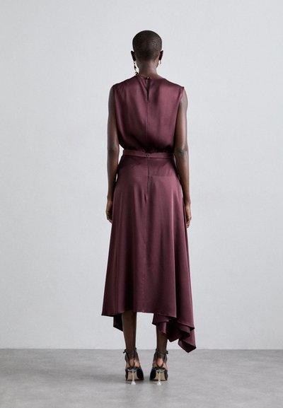 Burgundy satin dress with a sleeveless design, high-low hem, and belted waist, paired with strappy black heels.
