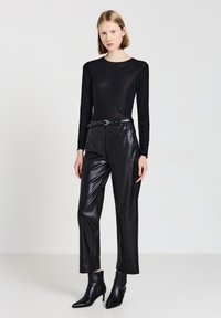 Schwarzes langärmliges Oberteil mit strukturierten Punkten, kombiniert mit hochtaillierter schwarzer Lederhose und spitzen Stiefeletten, die eine schlanke Silhouette erzeugen.