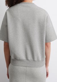 Szara bluza z mieszanki bawełny z opuszczonymi ramionami, ściągaczami na mankietach i luźnym fasonem. Minimalistyczne przeszycia z tyłu.