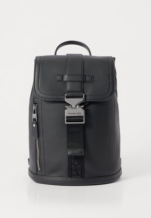 Sac à dos en cuir noir avec une finition texturée, fermeture à rabat, poche latérale zippée et quincaillerie métallique portant le nom de la marque.